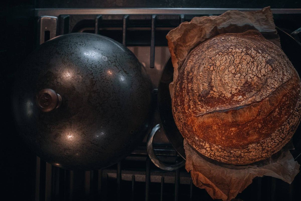 Domed carbon steel bread cloche cover and rustic sourdough boules in Dutch oven.
