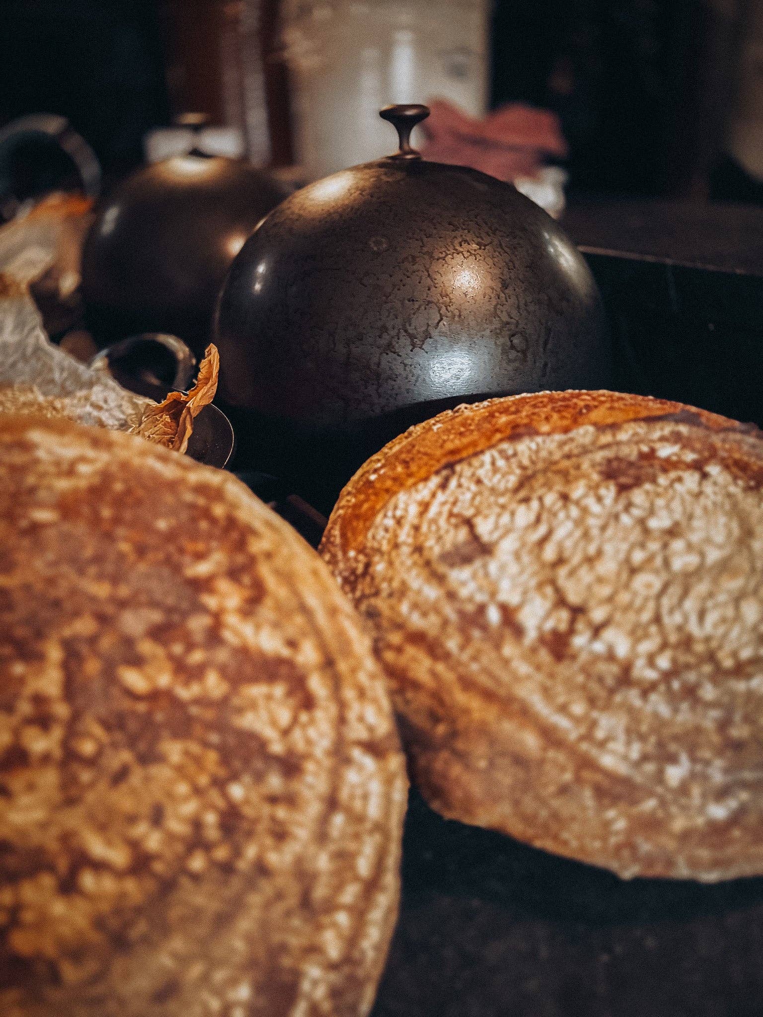 DOMED BREAD CLOCHE WITH RUSTIC LOAVES OF BOULE ON A DARK SURFACE