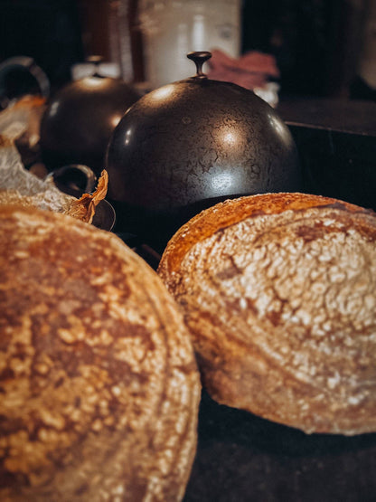 DOMED BREAD CLOCHE WITH RUSTIC LOAVES OF BOULE ON A DARK SURFACE