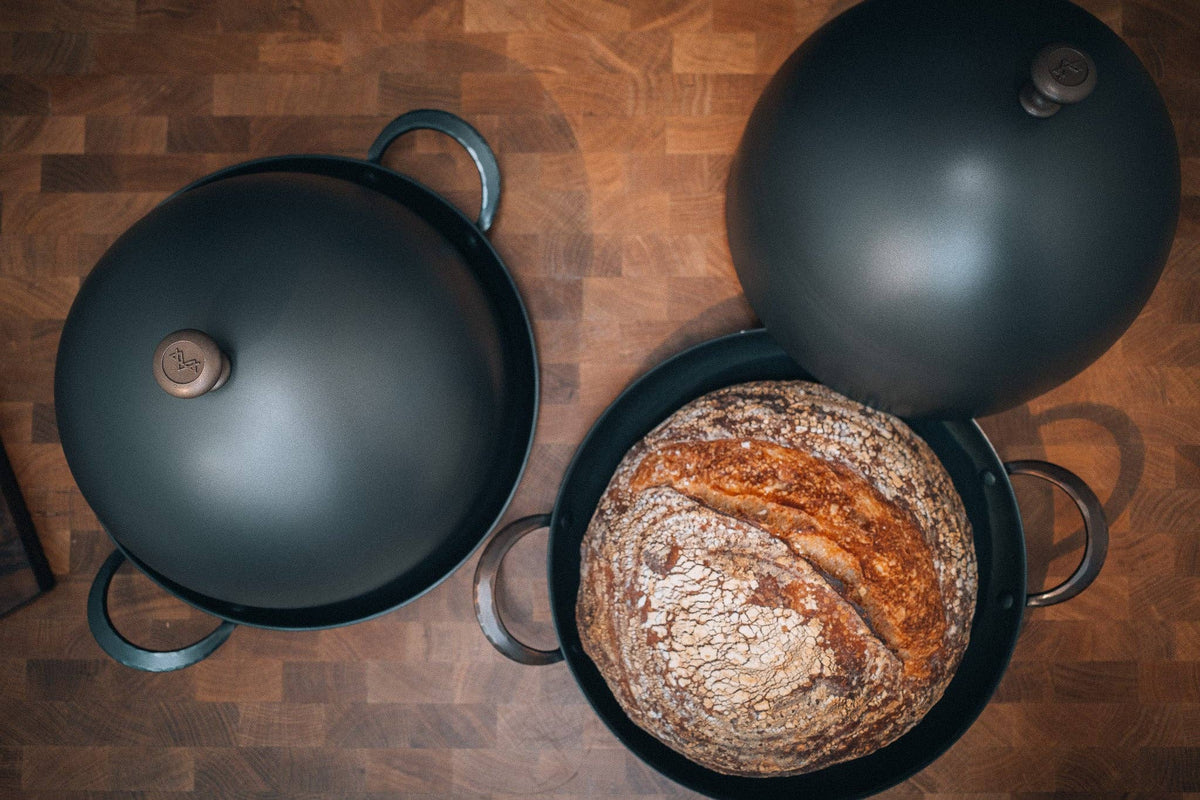 Bread Cloche and 11" roaster with rustic boule on wooden surface.